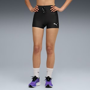 Against grey, a model poses in black Puma shorts, socks and purple running shoes.